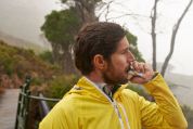 Bärtiger Mann in gelber Regenjacke isst einen Energieriegel. Bärtiger Mann in gelber Regenjacke isst einen Energieriegel.
